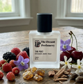 Perfume bottle labeled 'The Decant Perfumery' surrounded by fruits and flowers on a wooden surface.